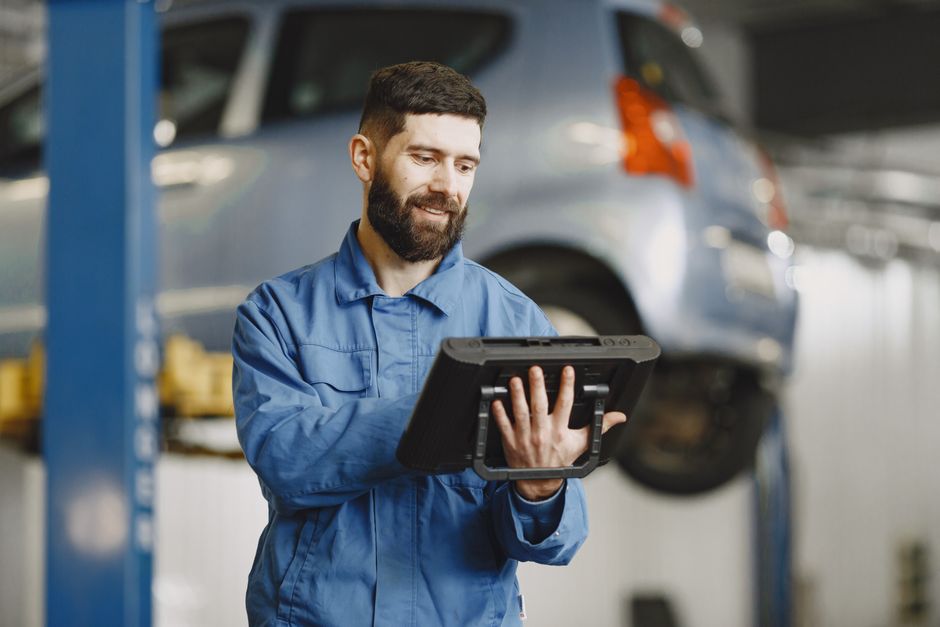 Smiling auto mechanic uses digital tablet in car repair shop environment.